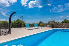 A swimming pool with two lounge chairs, a stone wall, and a clear blue sky. - Holiday house Lucy with private pool (Žgaljići (Krk))