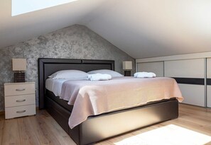 A modern bedroom with a sloped ceiling, a bed with white linens, a nightstand with a lamp, and a wooden floor. - Holiday house Lucy with private pool (Žgaljići (Krk))