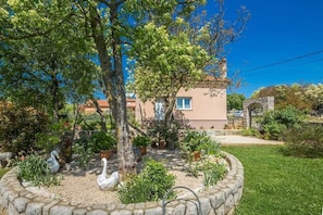 A garden with a stone fountain, swans, and a building in the background. - Holiday house Lucy with private pool (Žgaljići (Krk))