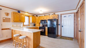 Una cocina con armarios de madera, una isla central con taburetes, un refrigerador negro y un microondas.