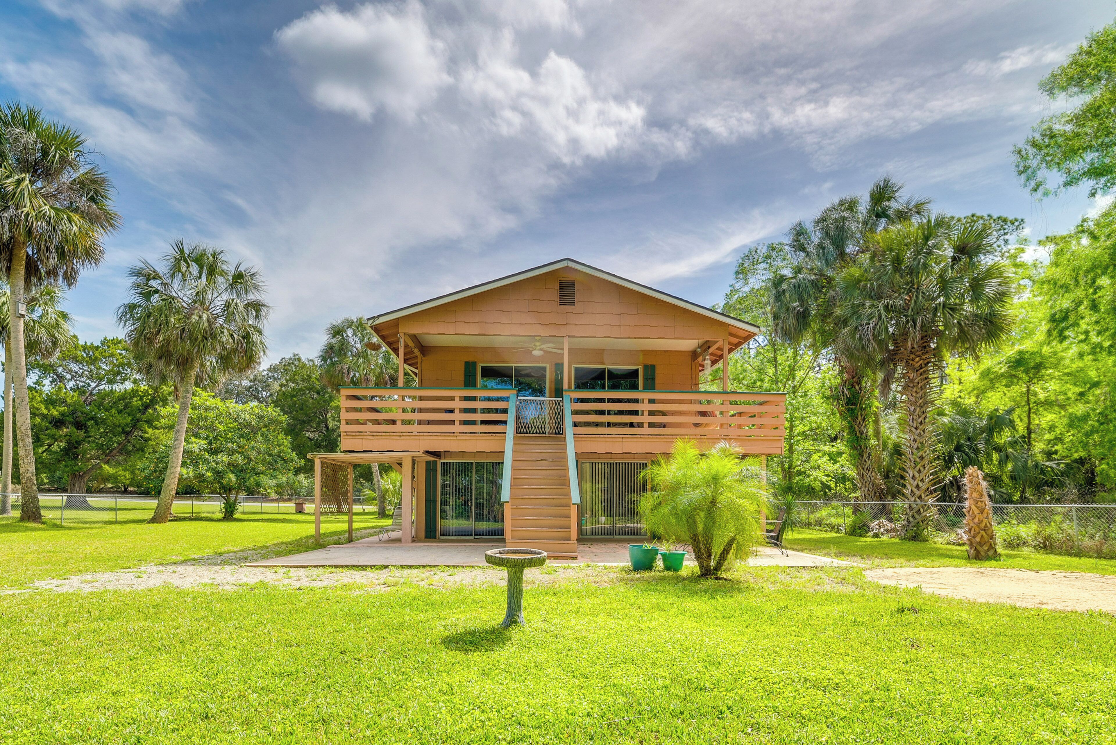 Una casa a due piani in legno, con un balcone, immersa nel verde e palme.