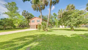 A single-story house with a red roof, surrounded by a well-maintained lawn and several palm trees. - Shared Dock & Fire Pit: Withlacoochee River Gem! (Inglis)