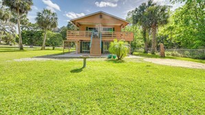 A two-story wooden house with a balcony, surrounded by a well-maintained lawn and palm trees. - Shared Dock & Fire Pit: Withlacoochee River Gem! (Inglis)