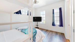 A room with bunk beds, a flat-screen TV, and large windows with curtains.