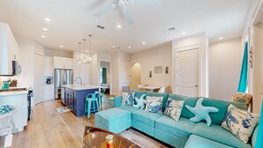 A modern living room with a teal sofa, a glass coffee table, and a ceiling fan.