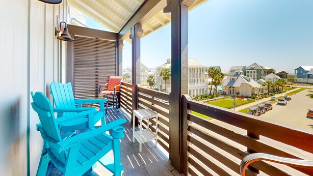 A balcony with a wooden railing, a blue Adirondack chair, a small table, and a white chair.