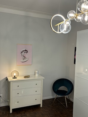 A modern room with a white dresser, a blue chair, a pendant light, and a framed picture on the wall.