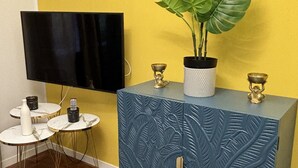 A room with a blue cabinet, a potted plant, a flat-screen TV, and two small round tables with decorative items. - Elegant Apartment Near Metro Line B - Luiss Guido Carli (Roma)