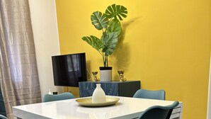 A dining area with a white table and teal chairs, a potted plant, and a TV on a stand. - Elegant Apartment Near Metro Line B - Luiss Guido Carli (Roma)