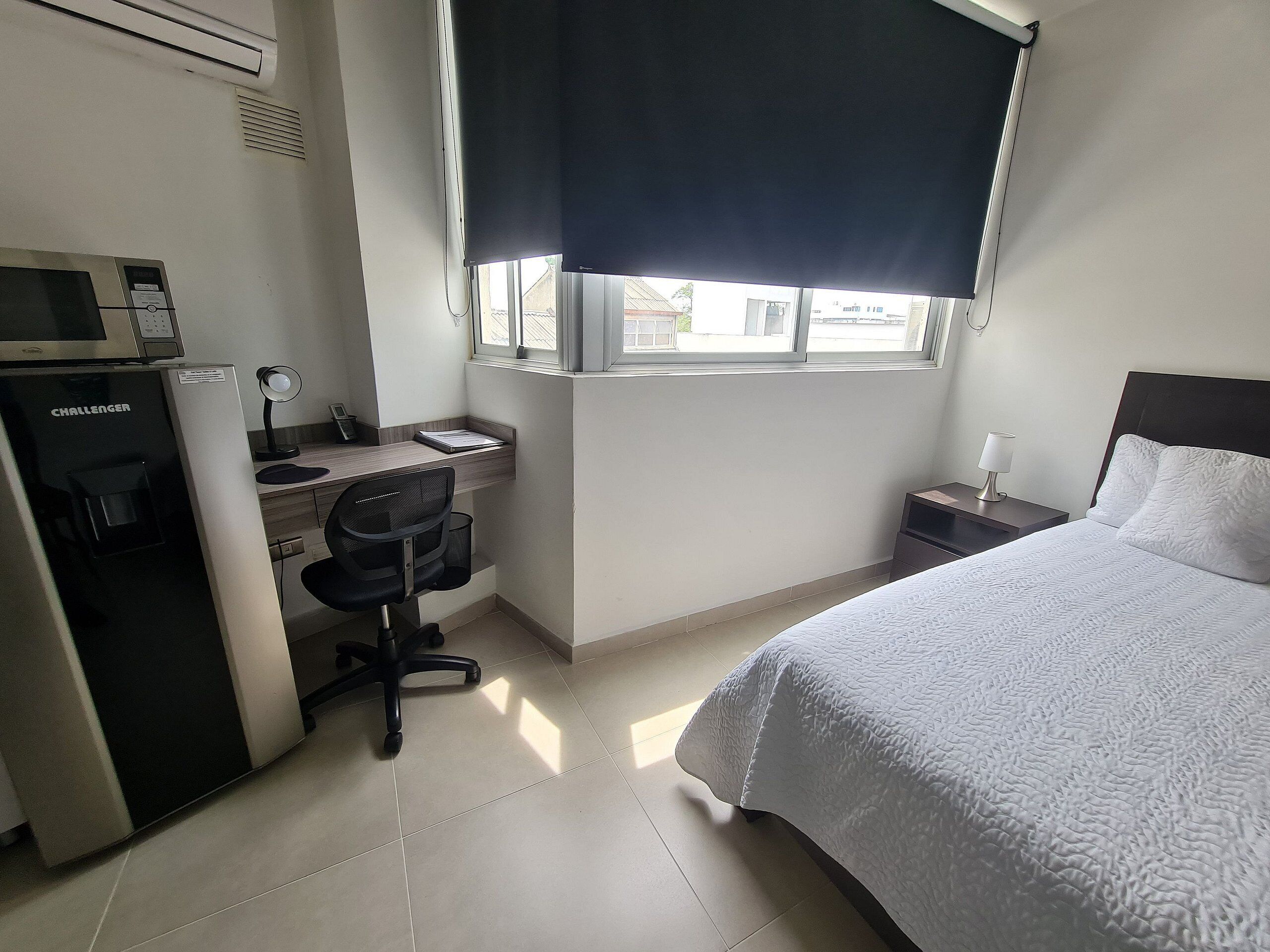 Una camera d'albergo con un letto, una scrivania con un computer, una sedia, una macchina per il caffè e una finestra con persiana.