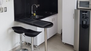 Une cuisine moderne avec un plan de travail noir, des armoires blanches, un four à micro-ondes encastré et une machine à café. On y trouve deux tabourets de bar et des luminaires suspendus au-dessus du plan de travail.