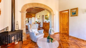 A spacious living area with a fireplace, a comfortable armchair, and a dining area in the background. - Can Juanito by dracmallorca (Cala Llombards)