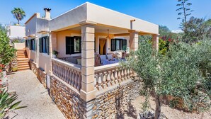A Mediterranean-style villa with a covered outdoor seating area, stone walls, and a garden with olive trees. - Can Juanito by dracmallorca (Cala Llombards)