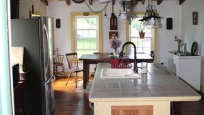 A kitchen with wooden floors, a central island with a sink, and hanging pots. - Historic Farmhouse in Chester County (Downingtown)