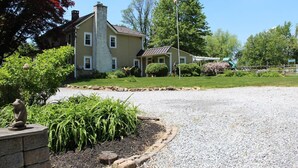 A two-story house with a front porch, a flagpole with an American flag, and a gravel driveway. - Historic Farmhouse in Chester County (Downingtown)