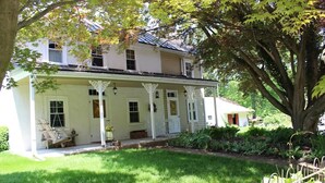 A two-story house with a porch, a swing chair, and a garden. - Historic Farmhouse in Chester County (Downingtown)