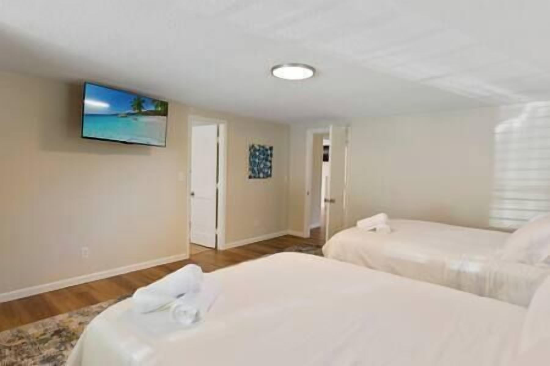 Ein Hotelzimmer mit zwei Betten, einem an der Wand befestigten Fernseher und einer Tür zu einem weiteren Raum.