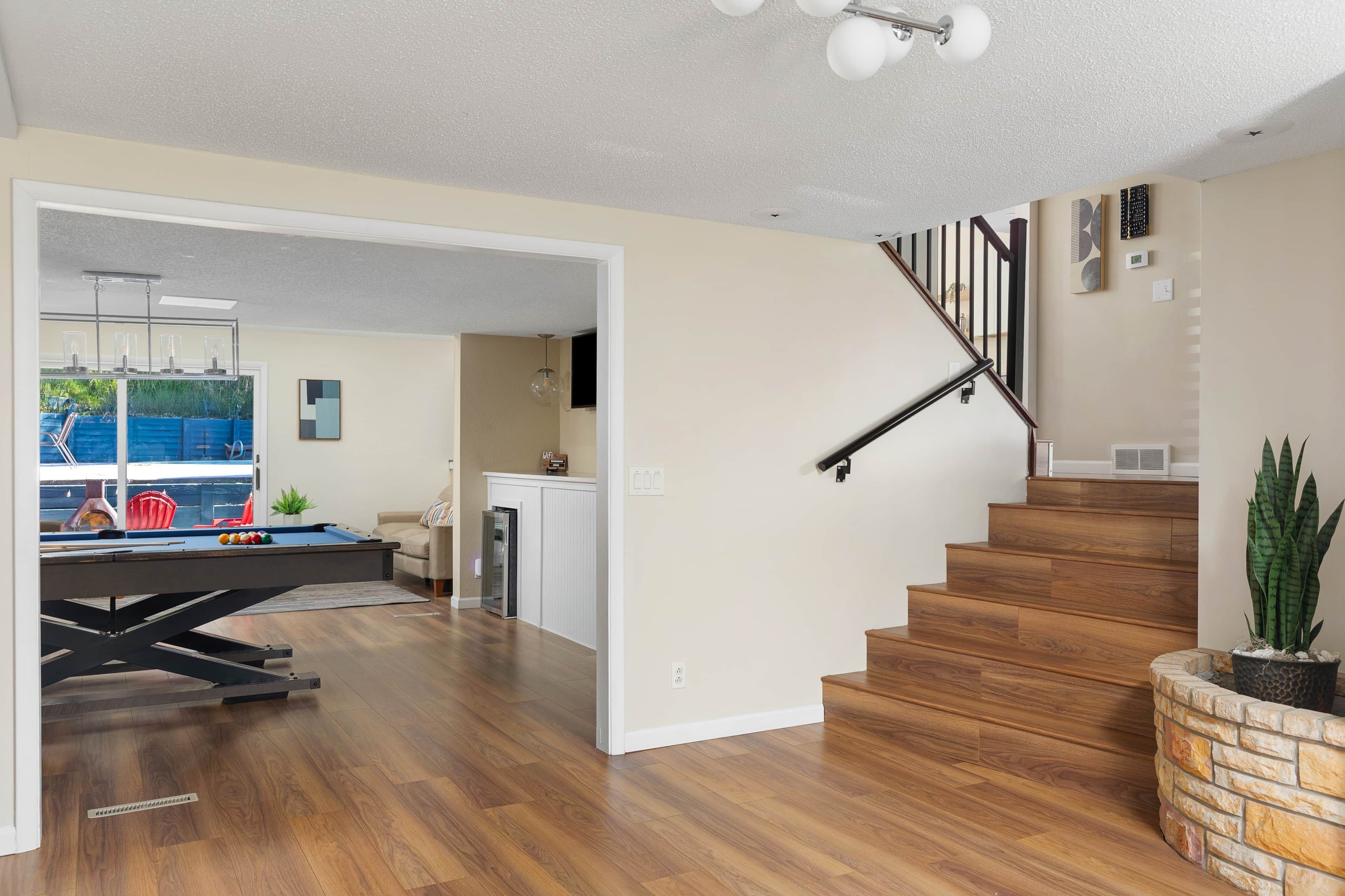 Un vaste espace de vie doté d’un plancher en bois, d’une table de billard et d’un escalier avec une rampe noire.