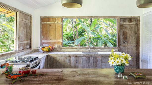 Una cocina con armarios de madera, una estufa a gas y un ventanal con vista a zonas verdes.