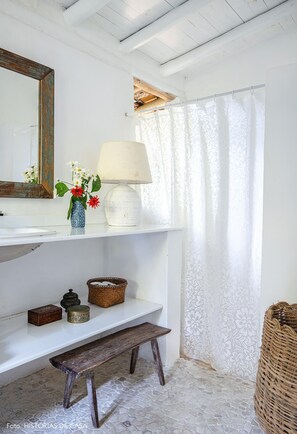 A bathroom with a white sink, mirror, and shelves holding a vase, lamp, and baskets. - Casas da Lia (Porto Seguro)