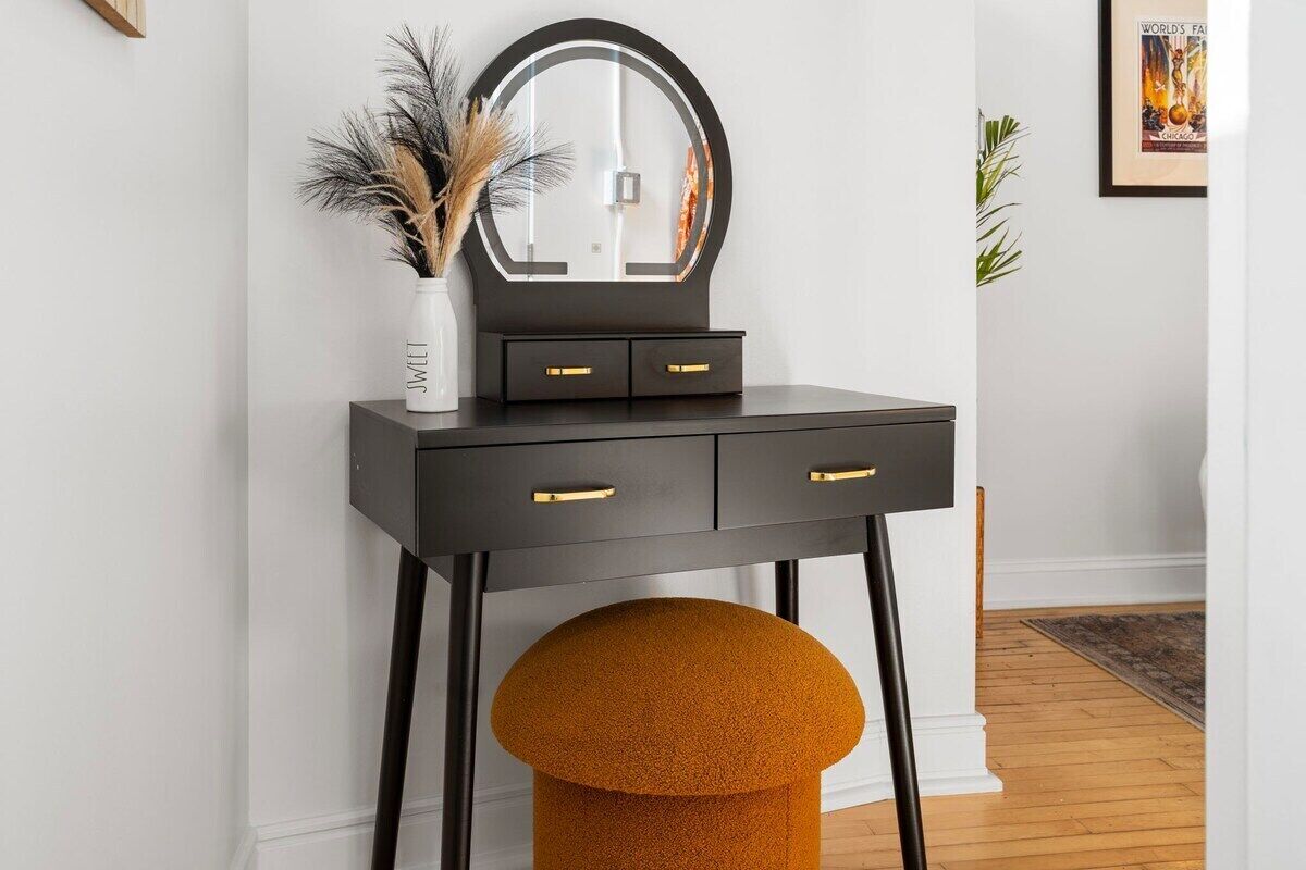 A black vanity with a round mirror, two drawers, and a stool.