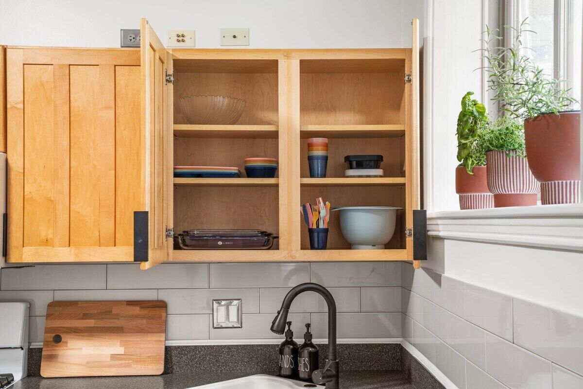 Una cocina con armarios de madera, una encimera, un lavabo con grifo y plantas en macetas en el alféizar.