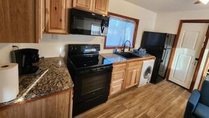 A compact kitchen with wooden cabinets, a microwave, an oven, a sink, and a washing machine. - Tiny home with cabin vibes (Nampa)