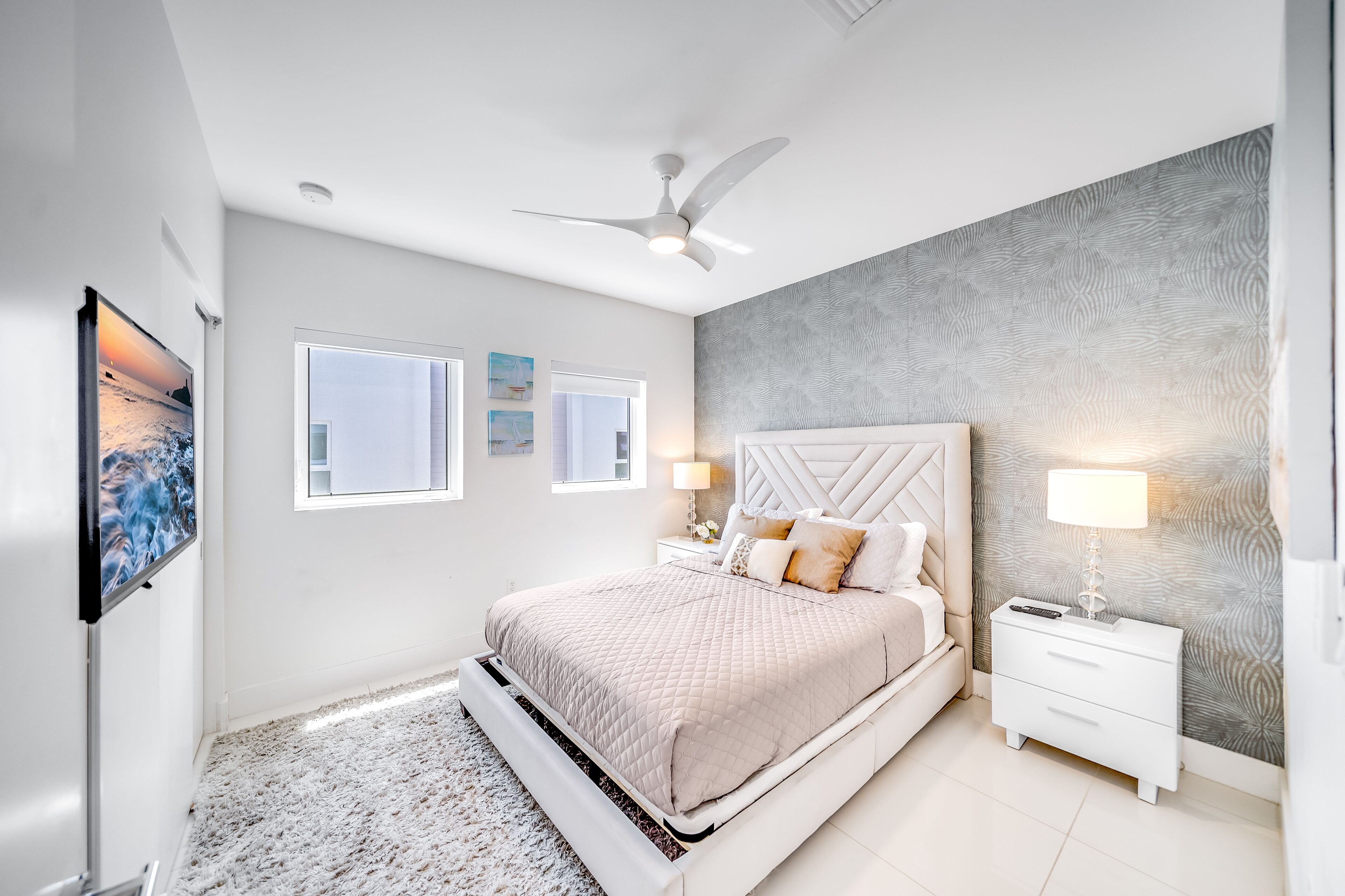 A modern bedroom with a bed, nightstands, a ceiling fan, and artwork on the walls.