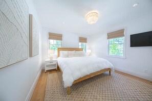 Ein Schlafzimmer mit einem hölzernen Bett, weißen Wänden und einem großen Fenster mit Jalousien.