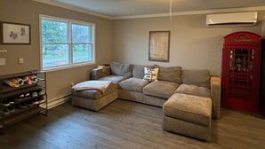 A living room with a sectional sofa, a ceiling fan, a shoe rack, a window, and a red telephone booth.