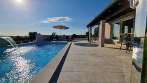 A swimming pool with a water feature, lounge chairs, and a covered seating area with tables and chairs. - Beautiful newly built villa with private pool in a small village in Istria (Sveti Petar u Šumi)