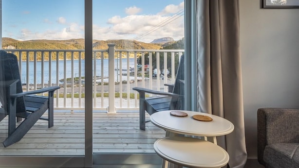 A balcony with a view of a lake and mountains, two Adirondack chairs, a small round table with coasters, and a grey sofa. - The Tides Inn (Norris Point)