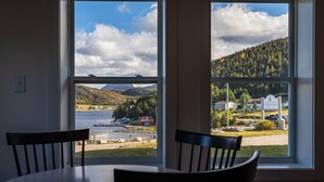 A room with a large window offering a view of a lake, a dock, and a red barn. - The Tides Inn (Norris Point)