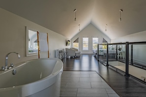 A spacious room with a large bathtub, a dining area with patterned chairs, and a balcony with a view.