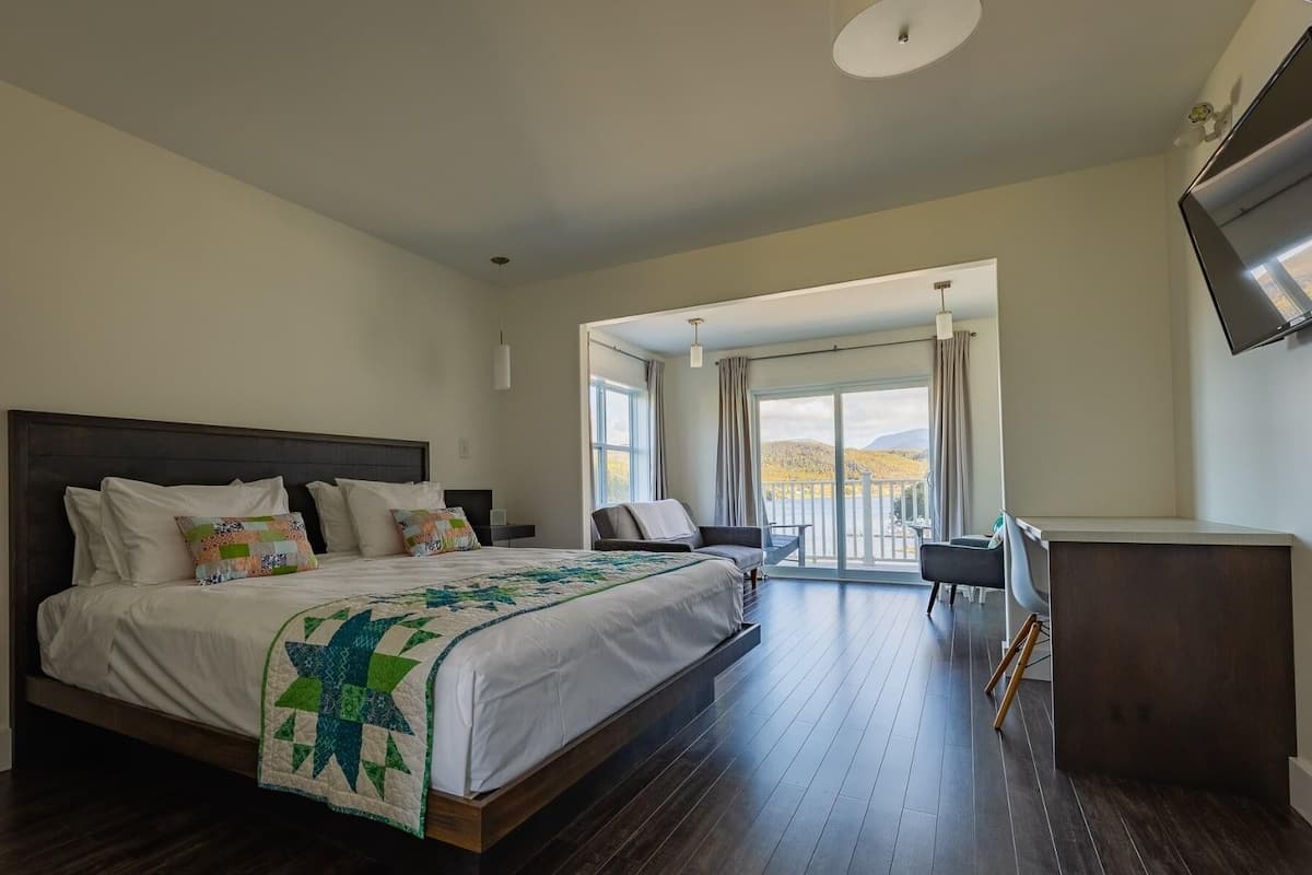 A bedroom with a large bed, a desk, and a balcony with a view.