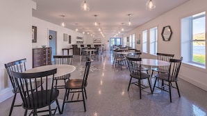 A spacious dining area with multiple tables and chairs, a bar area, and large windows offering a view. - The Tides Inn (Norris Point)