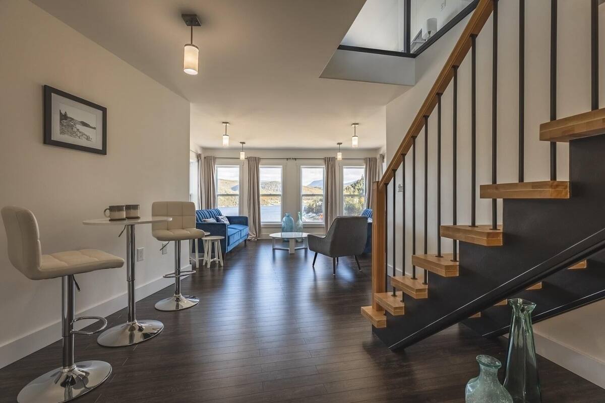 A spacious living area with a modern staircase, a dining area with bar stools, and a sofa set.