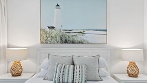 Une chambre à coucher avec un grand lit, deux tables de chevet et un tableau représentant un phare accroché au mur.