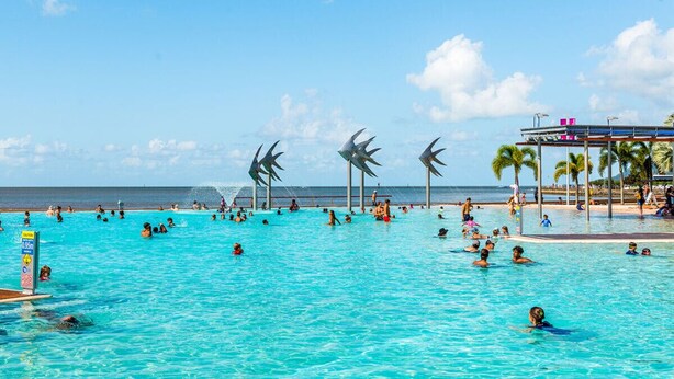 Une grande piscine extérieure où plusieurs personnes nagent et se détendent au bord de l’eau.
