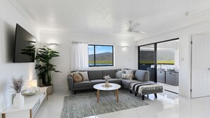 Un salon moderne avec un canapé gris, une table basse blanche et une grande fenêtre donnant sur l’extérieur.