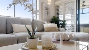 A modern living room with a grey sofa, a white orchid plant, a candle, and a decorative item on a glass table.