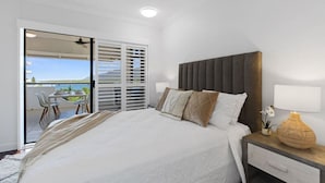 A bedroom with a bed, bedside table, lamp, and a view of the outdoors through a sliding door.
