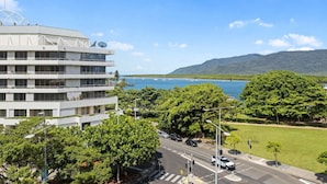 A multi-story building with balconies overlooking a coastal area with trees and a clear sky.