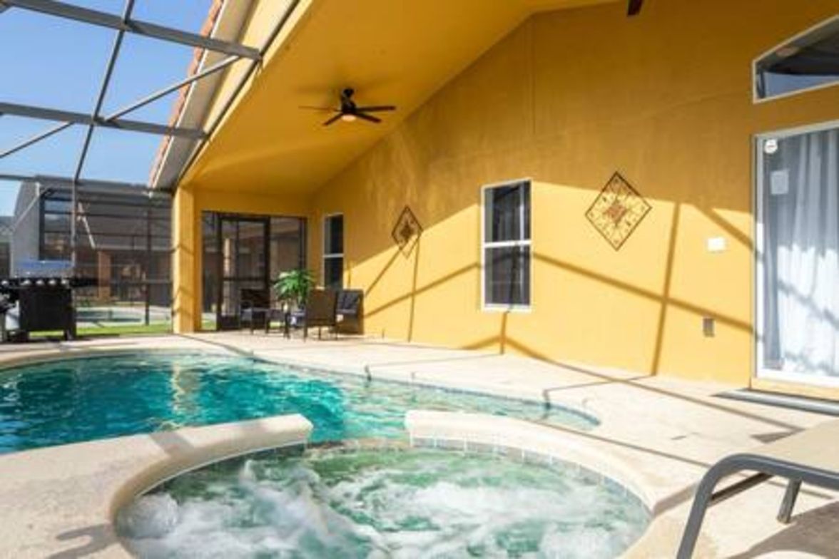 A pool area with a hot tub, outdoor seating, and a ceiling fan.