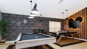 Una mesa de billar en una habitación con pared de ladrillo, televisor montado y pared de madera decorativa.
