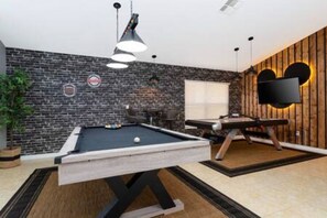 Ein Billardtisch in einem Raum mit Backsteinwand, einem an der Wand befestigten Fernseher und einer Wand mit Holzvertäfelung.