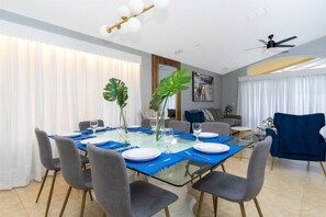 A dining area with a glass table, grey upholstered chairs, and a blue table runner. - 4BR Pool & Spa Home Near Disney (Kissimmee)