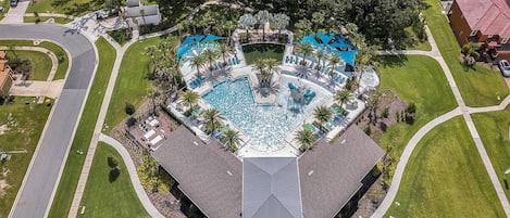 An aerial view of a resort with a central swimming pool, multiple lounge areas, and a symmetrical layout.