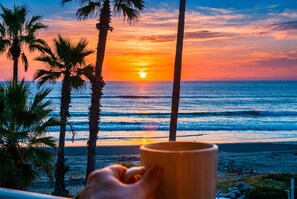 Atardecer sobre el océano con palmeras y una mano sosteniendo una taza.