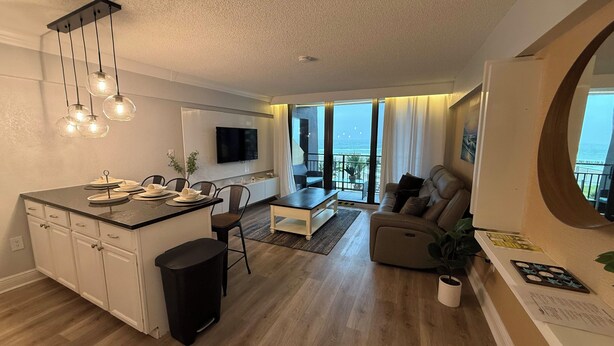 Una sala de estar moderna con comedor, una cocina con isla central y un balcón con vistas.